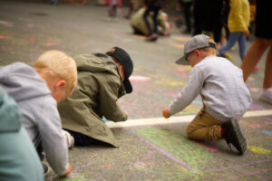 Kolme lasta piirtämässä liiduilla asfalttiin.